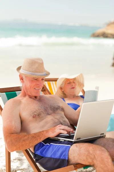 Plajda karısını okurken onun dizüstü bilgisayarda çalışan adam — Stok fotoğraf