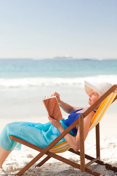 Oudere vrouw lezen van een boek op het strand — Stockfoto