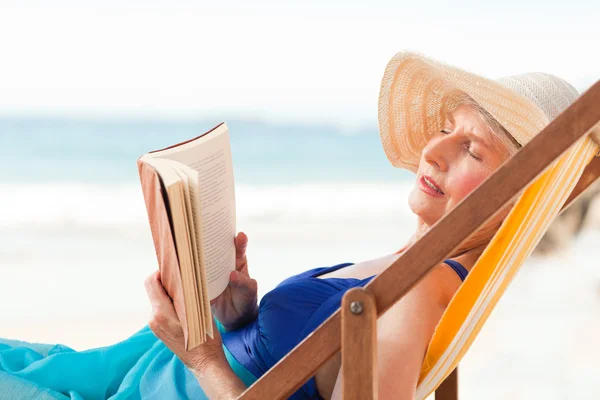 Mujer mayor leyendo un libro en la playa — Foto de Stock