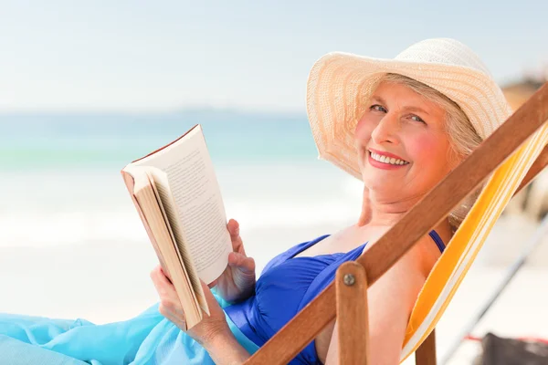 Ηλικιωμένη γυναίκα διαβάζοντας ένα βιβλίο στην παραλία — Φωτογραφία Αρχείου