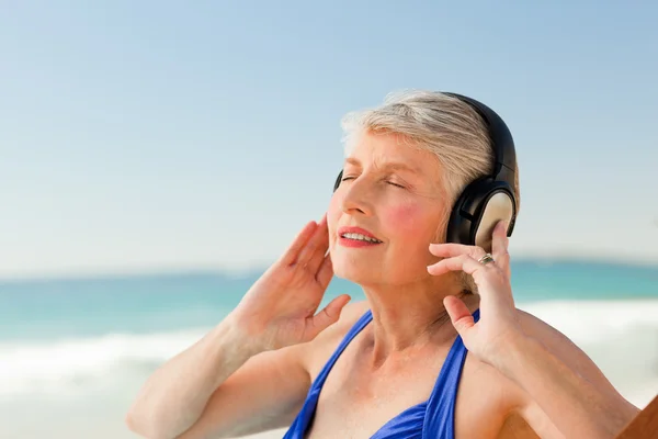 听音乐在海滩的高级女子 — 图库照片