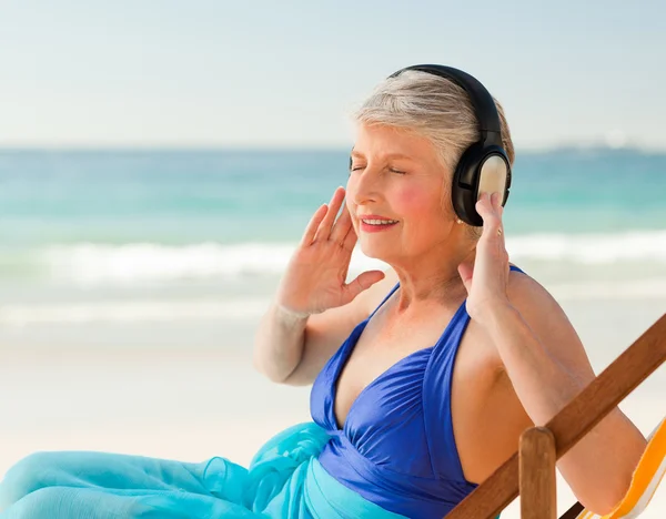 听音乐在海滩的退休的女士 — 图库照片
