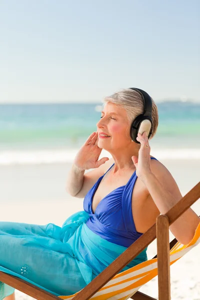 听音乐在海滩的退休的女士 — 图库照片