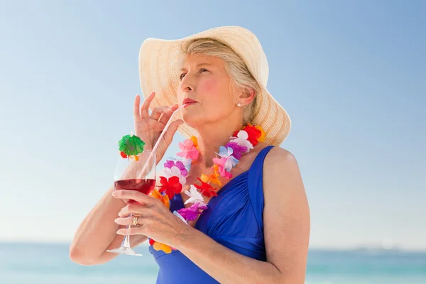 Літня жінка п'є коктейль на пляжі — стокове фото