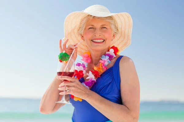 Oudere vrouw drinken een cocktail op het strand — Stockfoto