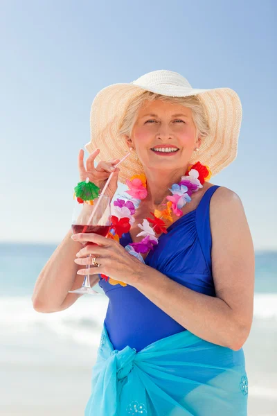 Elderly woman drinking a cocktail on the beach — Stock Photo, Image