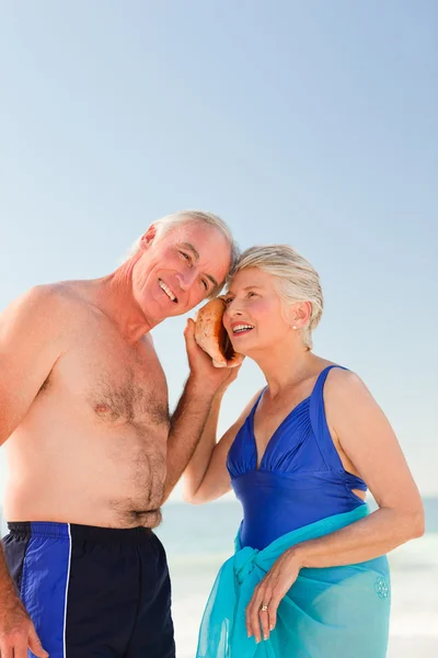 Retired couple listening to their shell — Stock Photo, Image