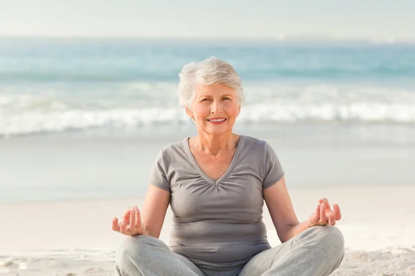 Äldre kvinna utövar yoga på stranden — Stockfoto