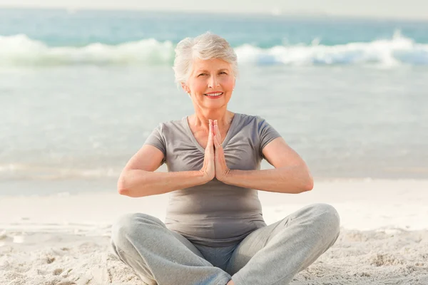 Mulher sênior praticando ioga na praia — Fotografia de Stock