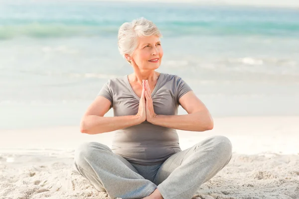 Starší žena cvičí jógu na pláži — Stock fotografie