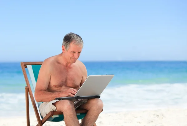 Uomo in pensione che lavora al suo portatile sulla spiaggia — Foto Stock