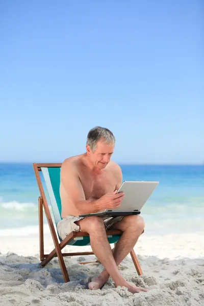 Пенсионер, работающий над ноутбуком на пляже — стоковое фото