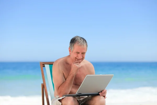Nyugdíjas ember dolgozik a laptop a strandon — Stock Fotó