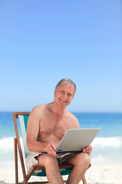 Kumsalda yaptığı dizüstü bilgisayarda çalışan emekli adam — Stok fotoğraf