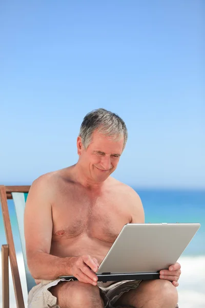 Kumsalda yaptığı dizüstü bilgisayarda çalışan emekli adam — Stok fotoğraf