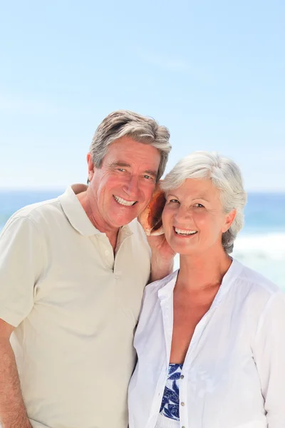 Retired couple listening to their shell — Stock Photo, Image