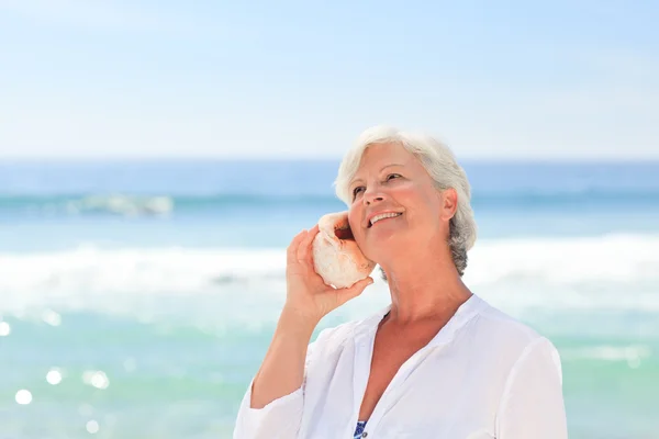 Mature woman listening to her shell — Stock Photo, Image