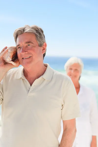 Man listening his shell with his wife behind him — Stock Photo, Image