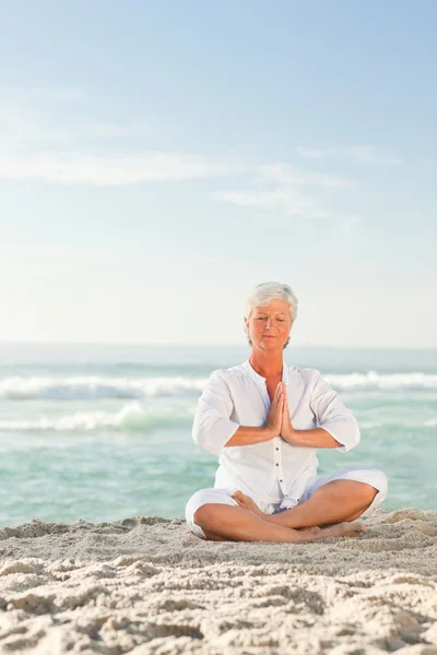 Mogen kvinna utövar yoga på stranden — Stockfoto