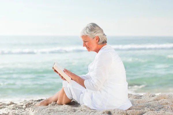 Oudere vrouw lezen van haar boek op het strand — Stockfoto