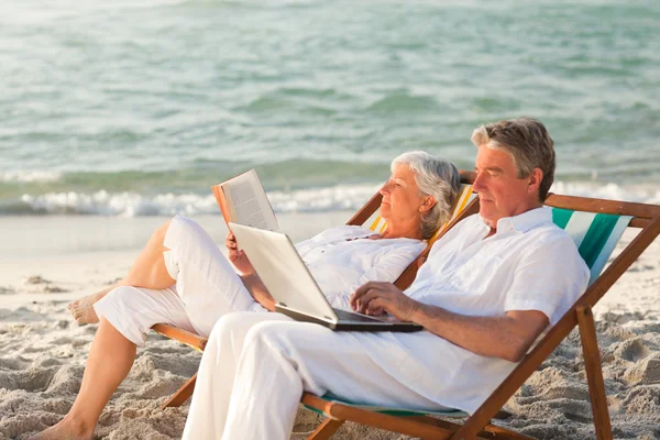 Mujer leyendo mientras su marido está trabajando en su portátil —  Fotos de Stock