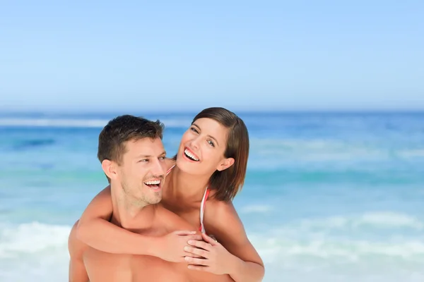 Bonito homem ter esposa um piggyback na praia — Fotografia de Stock