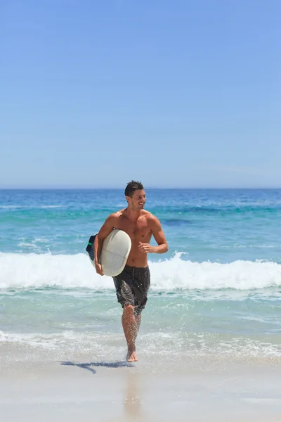 彼のサーフボードとビーチを走る男 — Stockfoto