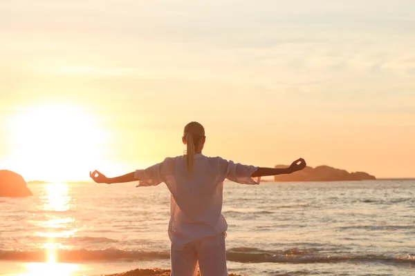 Mulher praticando ioga durante o pôr do sol na praia — Fotografia de Stock