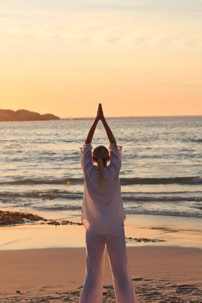 Женщина практикует йогу во время заката на пляже — стоковое фото