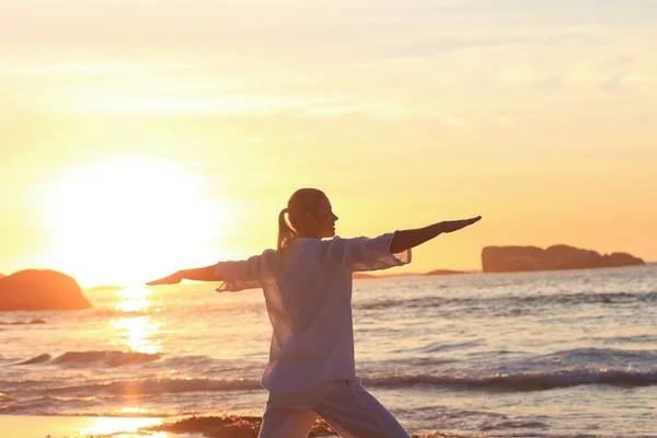 Vrouw beoefenen van yoga tijdens de zonsondergang op het strand — Stockfoto