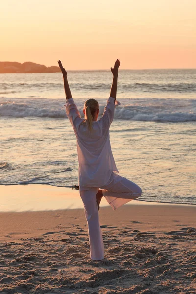 Frau praktiziert Yoga während des Sonnenuntergangs am Strand — Stockfoto