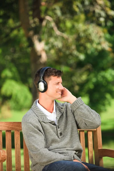 Молодой человек слушает музыку на скамейке — стоковое фото