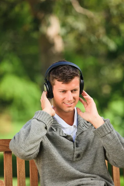 Молодой человек слушает музыку на скамейке — стоковое фото