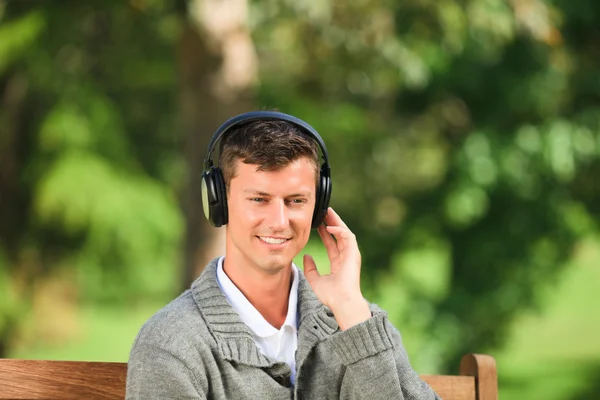 Jonge man luisteren naar muziek op de Bank — Stockfoto