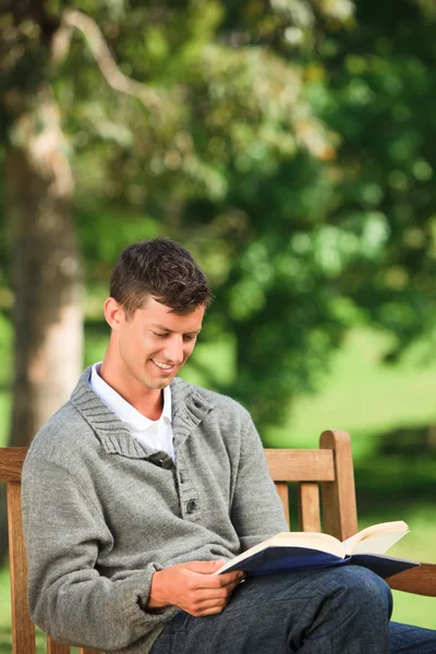 Νεαρός άνδρας, διαβάζοντας το βιβλίο του στον πάγκο — Φωτογραφία Αρχείου