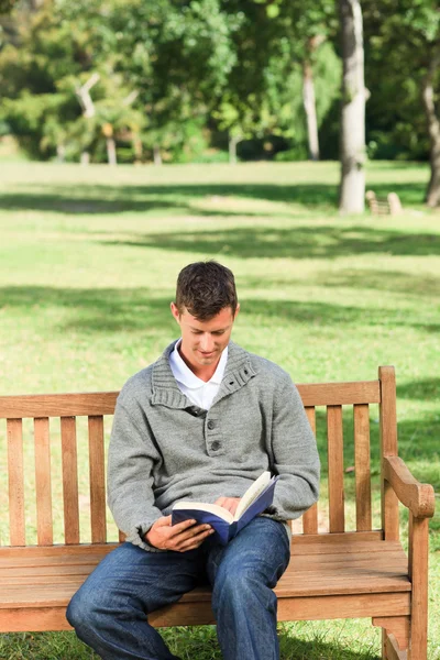 Mladý muž čtení jeho knihy na lavičce — Stock fotografie