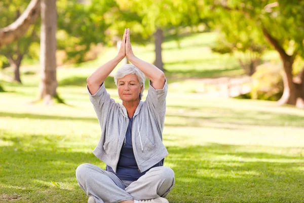 Starší žena cvičí jógu v parku — Stock fotografie