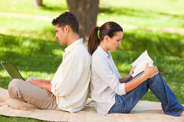 Homem trabalhando em seu laptop enquanto sua esposa está lendo — Fotografia de Stock
