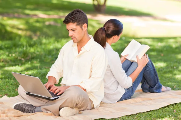 Man som arbetar på sin bärbara dator medan hans fru läser — Stockfoto