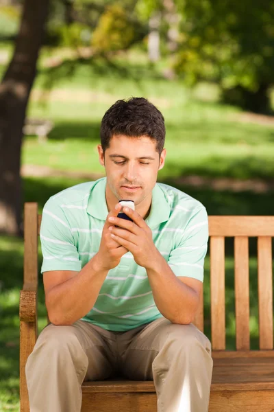 Человек со своим телефоном на скамейке запасных — стоковое фото
