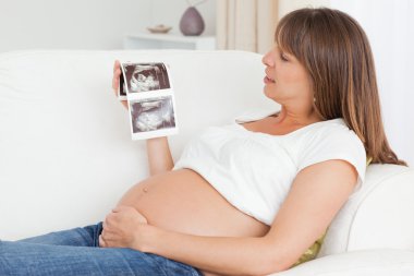 Happy pregnant woman looking at her baby's ultrasound scan clipart