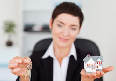 Businesswoman showing a miniature house and a key clipart