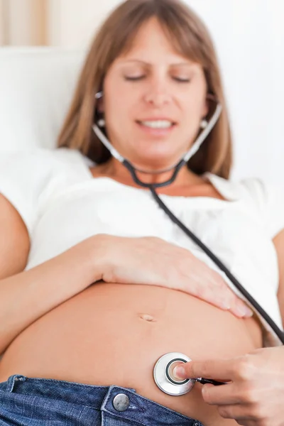 Geconfronteerd met uitzicht op een mooie zwangere vrouw met behulp van een stethoscoop wh — Stockfoto