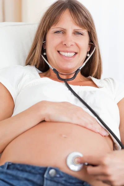 Vista frontal de una mujer embarazada de buen aspecto usando un estetoscopio —  Fotos de Stock