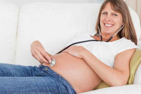 美しい妊娠中の女性に横たわっている間、聴診器を使用して、ので — ストック写真