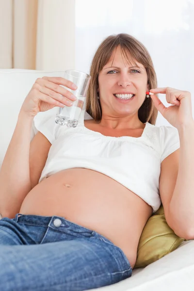 Hermosa mujer embarazada tomando una píldora mientras está acostada en un sofá —  Fotos de Stock