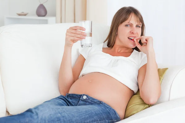 Очаровательная беременная женщина, принимающая таблетки, лежа на диване — стоковое фото