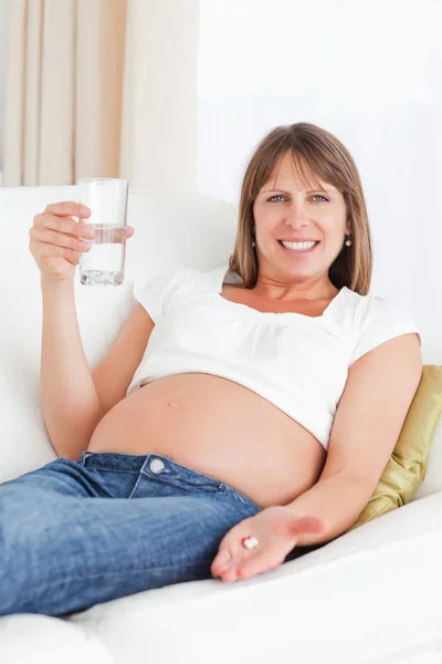 Ziemlich schwangere Frau nimmt eine Pille, während sie auf einem Sofa liegt — Stockfoto