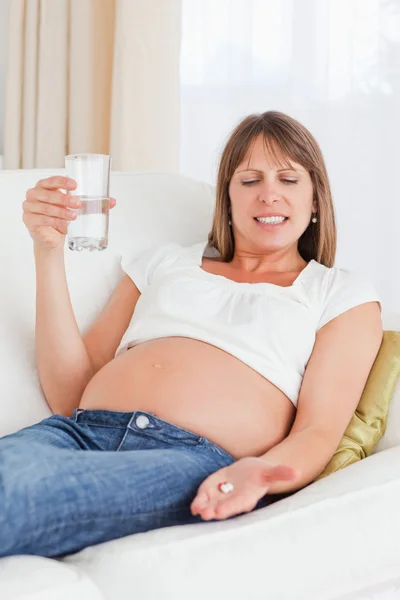 Attrayant femme enceinte prenant une pilule tout en étant couché sur un canapé — Photo