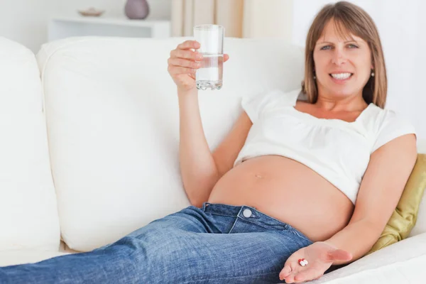 Süße schwangere Frau nimmt eine Pille, während sie auf dem Sofa liegt — Stockfoto
